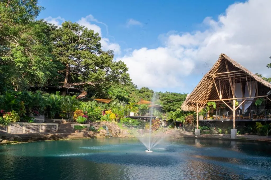 An open-air thatched gathering pavilion at TreeCasa with a fountain pond in front and the jungle behind